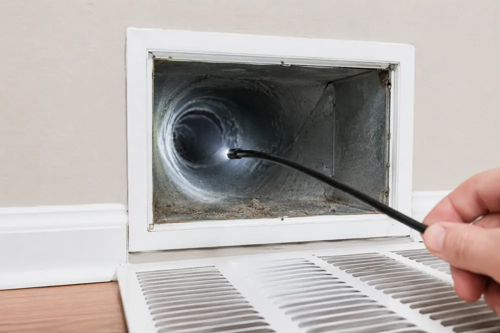 Technician inspecting an air duct with a camera scope through a wall vent