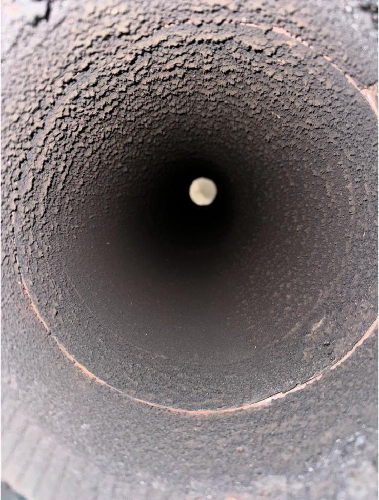 Round chimney flue coated in creosote before a professional chimney sweep in Dallas, TX
