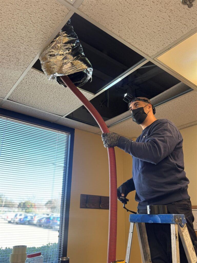 Warrior technician cleaning air ducts above a suspended ceiling in a Dallas office building